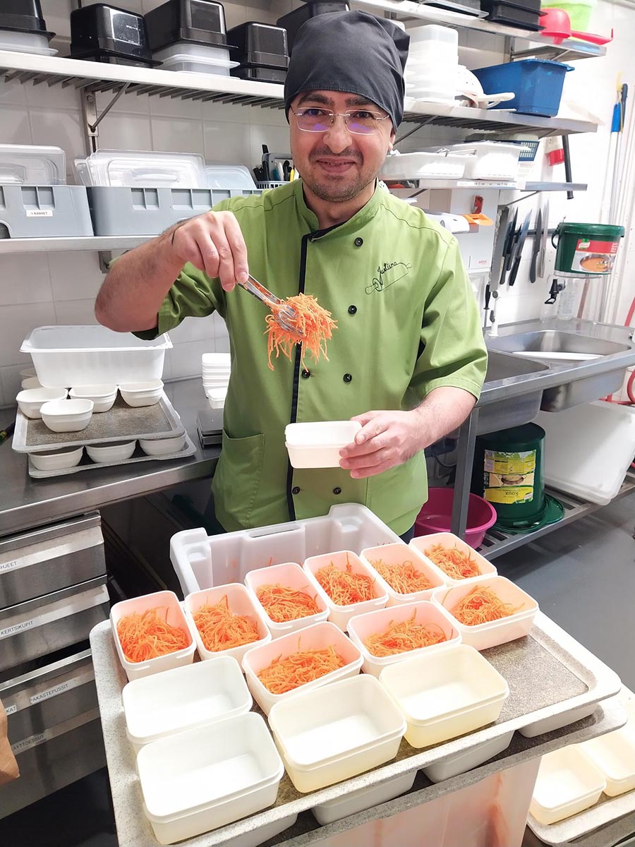 Justiina Ateriapalveluiden työntekijä Hasan Tosun annostelemassa porkkanasalaattia.